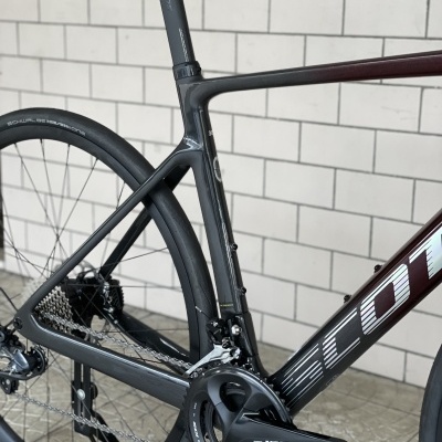 Detalhe da bicicleta de estrada Scott em carbono preto com sistema Shimano 105 e fundo de parede de azulejos claros