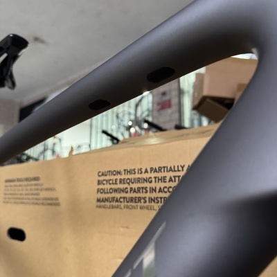 Quadro de bicicleta cinzento fosco com orifícios pretos e caixa de cartão ao fundo