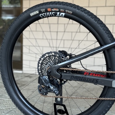 Roda traseira de bicicleta com pneu preto e quadro preto diante de parede de tijolos