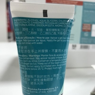 Tubo de gel branco e verde azulado com texto multilingue em fundo desfocado.