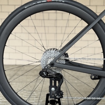 Roda traseira de bicicleta com pneu preto Schwalbe Pro One e quadro cinza em fundo de parede bege