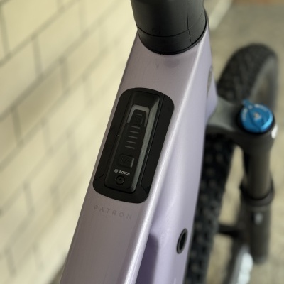 Bicicleta elétrica lilás com controlador Bosch embutido no quadro e garfo dianteiro preto com botão azul.