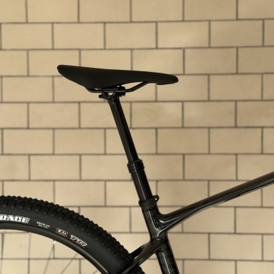 Parte traseira de bicicleta preta com selim e pneu, parede de tijolos ao fundo