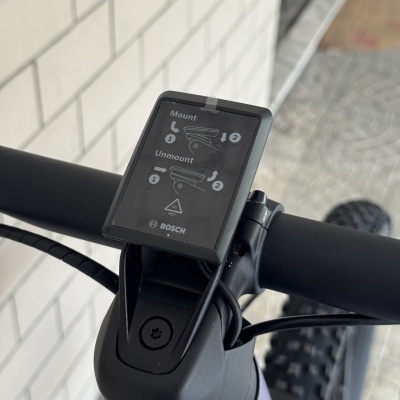 Mostrador digital Bosch no guiador de bicicleta com instruções e fundo branco de azulejos