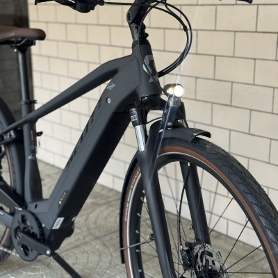 Bicicleta elétrica preta com farol dianteiro ligado e selim castanho