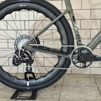 Roda traseira de bicicleta com pneu preto Schwalbe, aro preto, corrente e pedaleira preta SRAM FORCE, quadro verde, suporte SCOTT.
