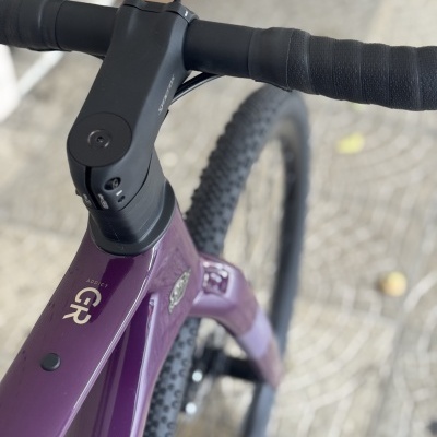 Guiador e parte do quadro de bicicleta roxa com pneus robustos e guiador preto