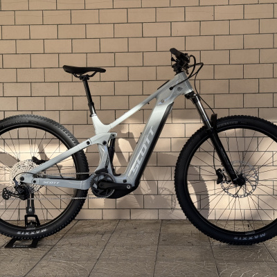 Bicicleta elétrica SCOTT cinzenta junto a parede de azulejos bege.
