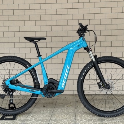 Bicicleta elétrica azul Scott junto a parede de tijolos cinza