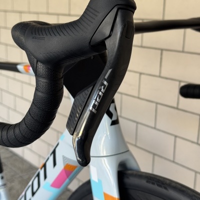 Punho de bicicleta preta com alavanca, guiador com fita preta e quadro branco colorido.