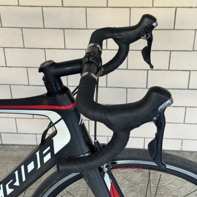 Parte dianteira de bicicleta estrada preta e vermelha com guiador em drop e travões Shimano 105.