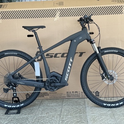 Bicicleta de montanha elétrica SCOTT com quadro cinza escuro sobre piso, caixa de cartão ao fundo
