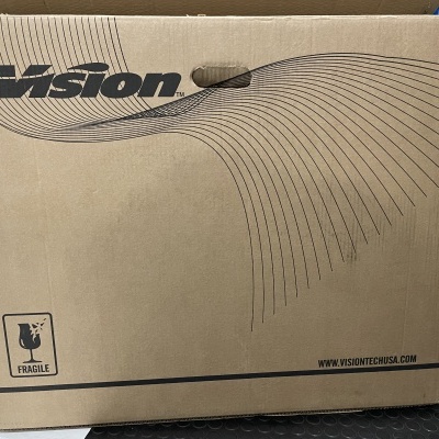 Caixa de cartão castanha com logótipo 'Vision', símbolo de 'FRAGILE' e URL na frente