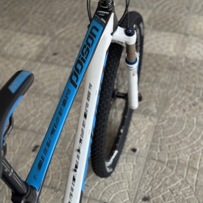 Bicicleta de montanha branca e azul com pneus pretos, suspensão dianteira e texto poison no quadro