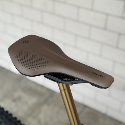 Selim de bicicleta castanho com palavra TOFINO e cana de selim dourada