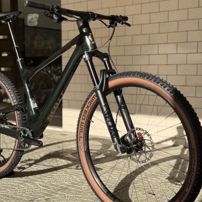 Bicicleta de montanha preta com pneus castanhos em piso de azulejos junto a parede de tijolos