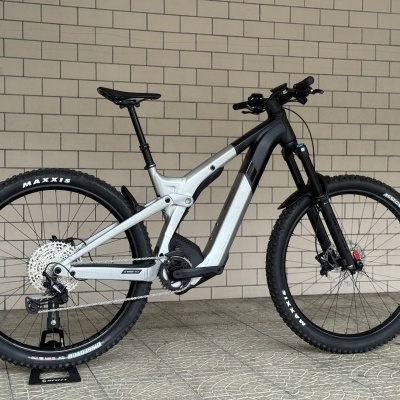 Bicicleta de montanha elétrica preta e cinza com pneus Maxxis, suspensões e em suporte