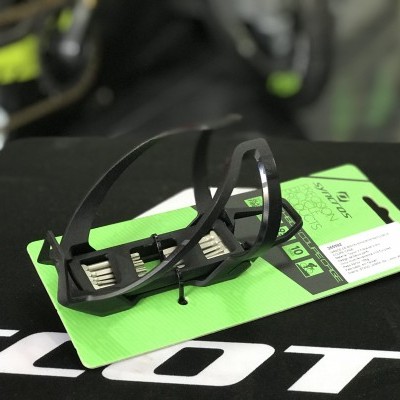 Suporte de bidão preto para bicicleta embalado numa cartolina verde sobre superfície preta com logótipo SCOTT