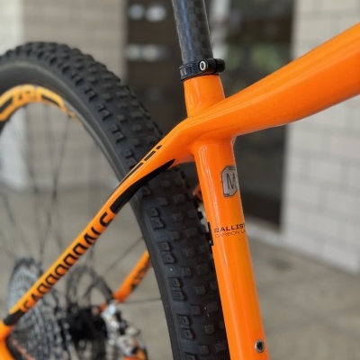 Bicicleta de montanha laranja com pneus de cravos pretos e detalhes em carbono