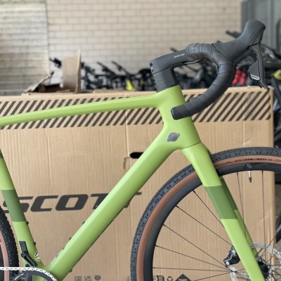 Bicicleta de estrada verde fosco com pneus castanho escuro numa caixa com logo SCOTT