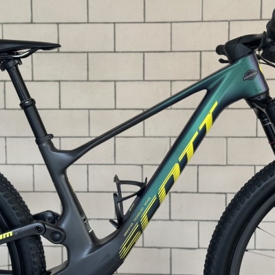 Bicicleta de montanha verde escuro e preto com detalhes amarelos e suspensão Rock Shox.