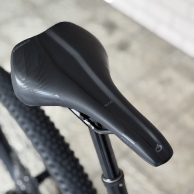 Selim de bicicleta preto com texto PROLOGO e AGX montado em suporte preto sobre chão cinzento desfocado