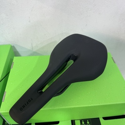 Selim de bicicleta preto com corte central e caixas verdes ao fundo.