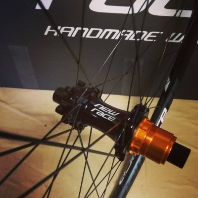 Roda de bicicleta com cubo preto e eixo laranja metálico, raios pretos