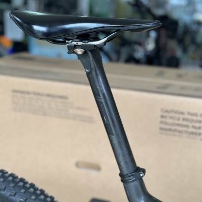 Selim preto e canote de carbono de bicicleta com caixa de papelão ao fundo.