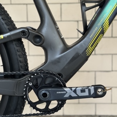 Bicicleta todo-o-terreno com quadro cinza escuro e detalhes amarelos, pedaleiro SRAM X01 e corrente preta