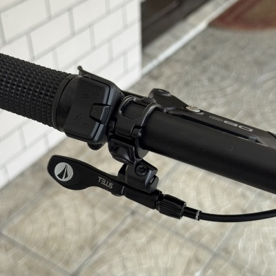 Punho e manete do guiador de uma bicicleta preta com inscrições TELLIS e símbolos de controlo de luzes