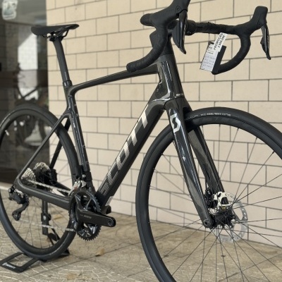 Bicicleta de estrada SCOTT em carbono preto e cinza com pneus Schwalbe One e etiqueta de promoção