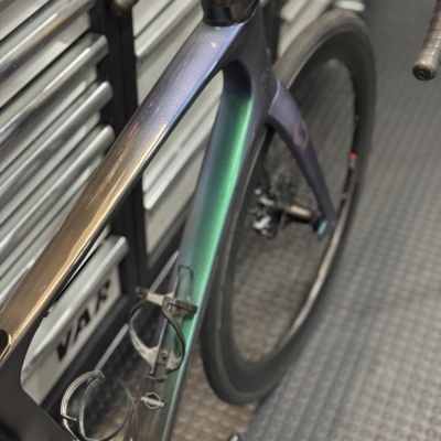 Bicicleta de estrada cor metálica azul, verde e roxo com guiador preto e roda preta em oficina com armário de ferramentas