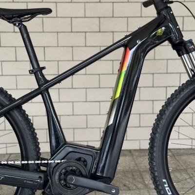 Bicicleta elétrica de montanha preta com detalhes coloridos em parede clara