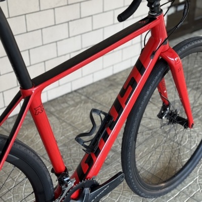 Bicicleta de estrada vermelha e preta num ambiente exterior com parede branca e chão de pedra.