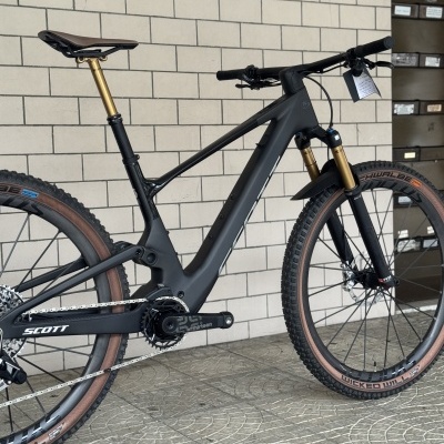 Bicicleta de montanha preta com detalhes dourados e pneus Schwalbe numa parede de azulejos brancos