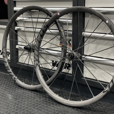 Duas rodas de bicicleta em carbono apoiadas no chão contra um armário metálico.