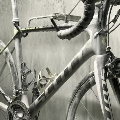 Bicicleta de estrada cinza com marca SCOTT e guiador envolto em fita preta, coberta de poeira