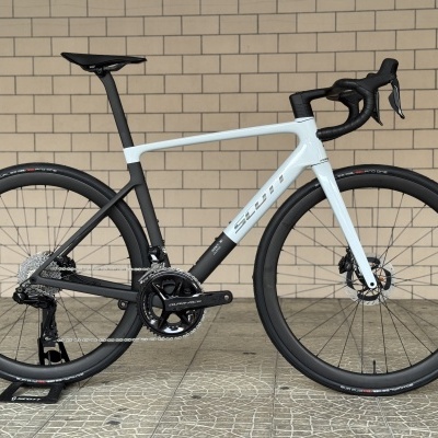 Bicicleta de estrada Scott branca e preta encostada numa parede de tijolos