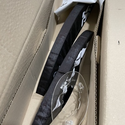 Peças negras com capa de tecido e base transparente em caixa de cartão aberta