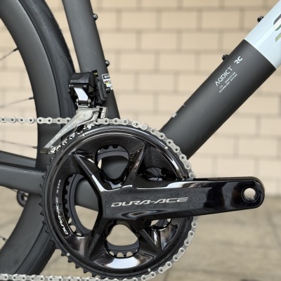 Pédalier DURA-ACE preto em bicicleta com quadro cinza e branco junto a parede de tijolos claros