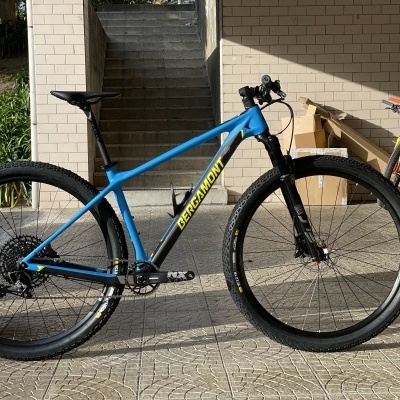 Bicicleta de montanha azul e preta em espaço coberto com paredes claras e escadas ao fundo