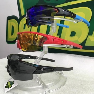 Três óculos desportivos coloridos em suporte transparente, com logótipo verde e amarelo ao fundo.