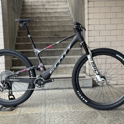 Bicicleta de montanha SCOTT preta com detalhes rosa e cinza apoiada num suporte no chão junto a escada e muro azulejado