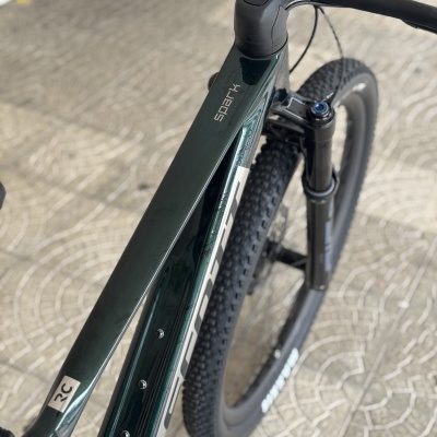 Bicicleta de montanha preta e verde escuro com pneus grossos sobre calçada