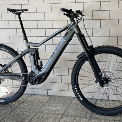 Bicicleta elétrica de montanha cinzenta junto a parede de azulejos brancos