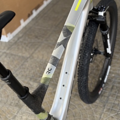 Bicicleta de montanha branca com detalhes pretos e verdes, pneu e selim preto sobre piso de mosaico cinzento.