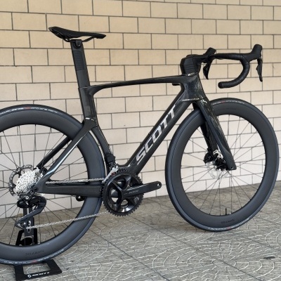 Bicicleta de estrada preta SCOTT em fibra de carbono encostada numa parede de tijolos claros