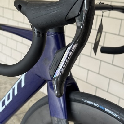 Punho de bicicleta de estrada preto com manete em carbono SRAM FORCE, quadro azul escuro e roda com pneu Schwalbe Pro One Aero