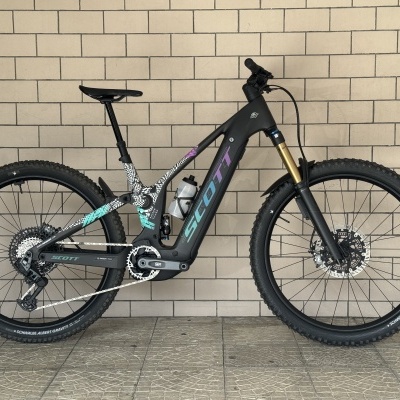 bicicleta de montanha elétrica Scott preta com detalhes coloridos encostada numa parede de tijolos